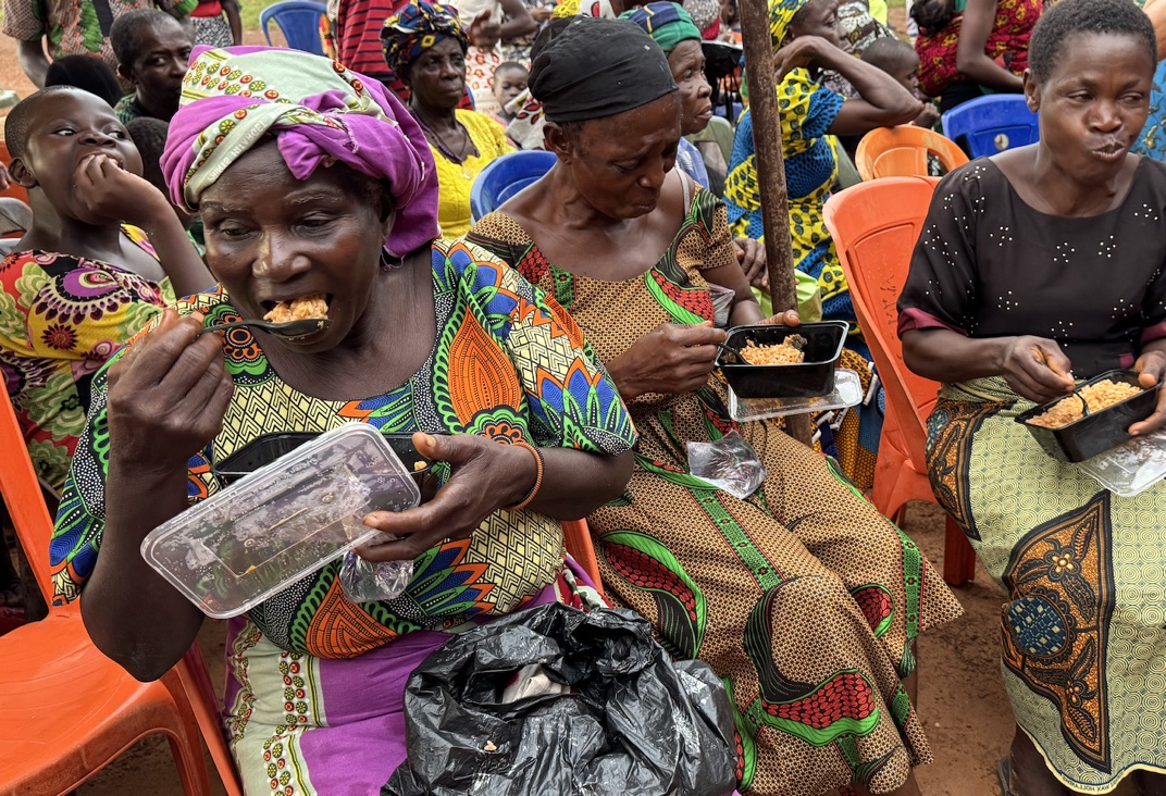 Widows in colorful traditional dress eating together at a community distribution day.